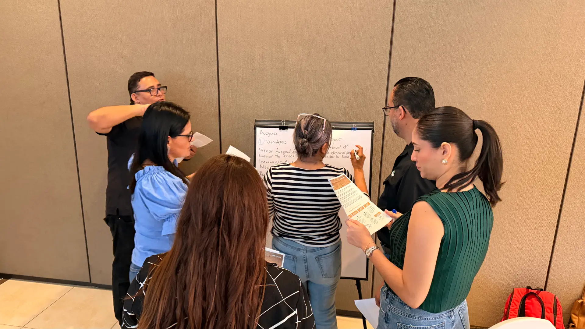 Participantes de un taller colaborando alrededor de un rotafolio